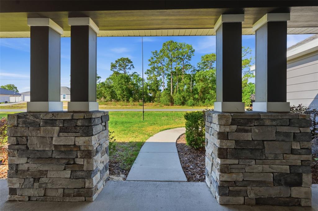 A view from a covered porch looking out toward a sidewalk, lawn, and distant trees — 5332 PIERPOINT AVENUE, SPRING HILL, FL