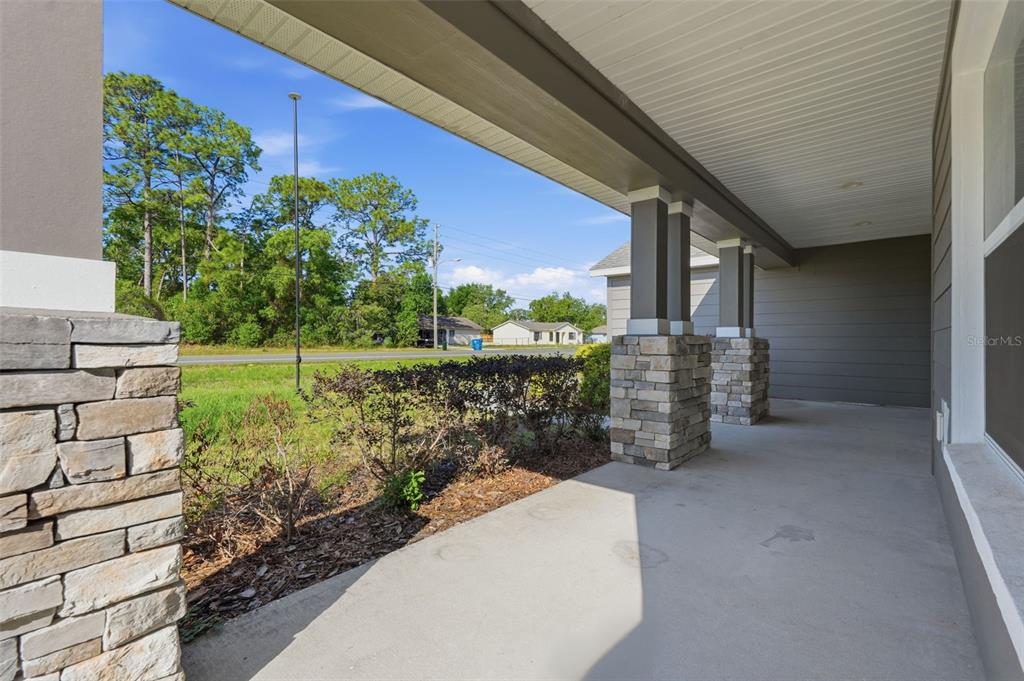 A covered concrete porch features stone-clad columns and a view of a grassy yard — 5332 PIERPOINT AVENUE, SPRING HILL, FL