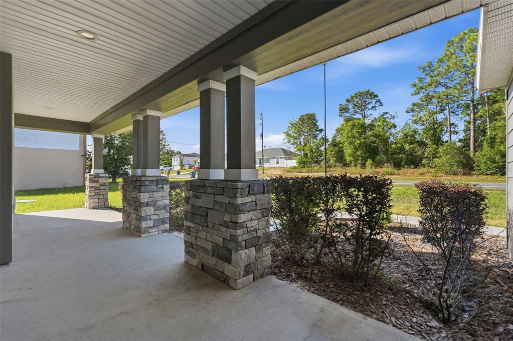 A covered concrete porch features stone-based columns and a view of a grassy yard — 5332 PIERPOINT AVENUE, SPRING HILL, FL