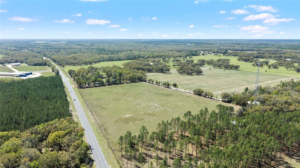 An aerial view shows a large, open grassy field bordered by forests and a road — 300 NE 708 AVENUE, OLD TOWN, FL