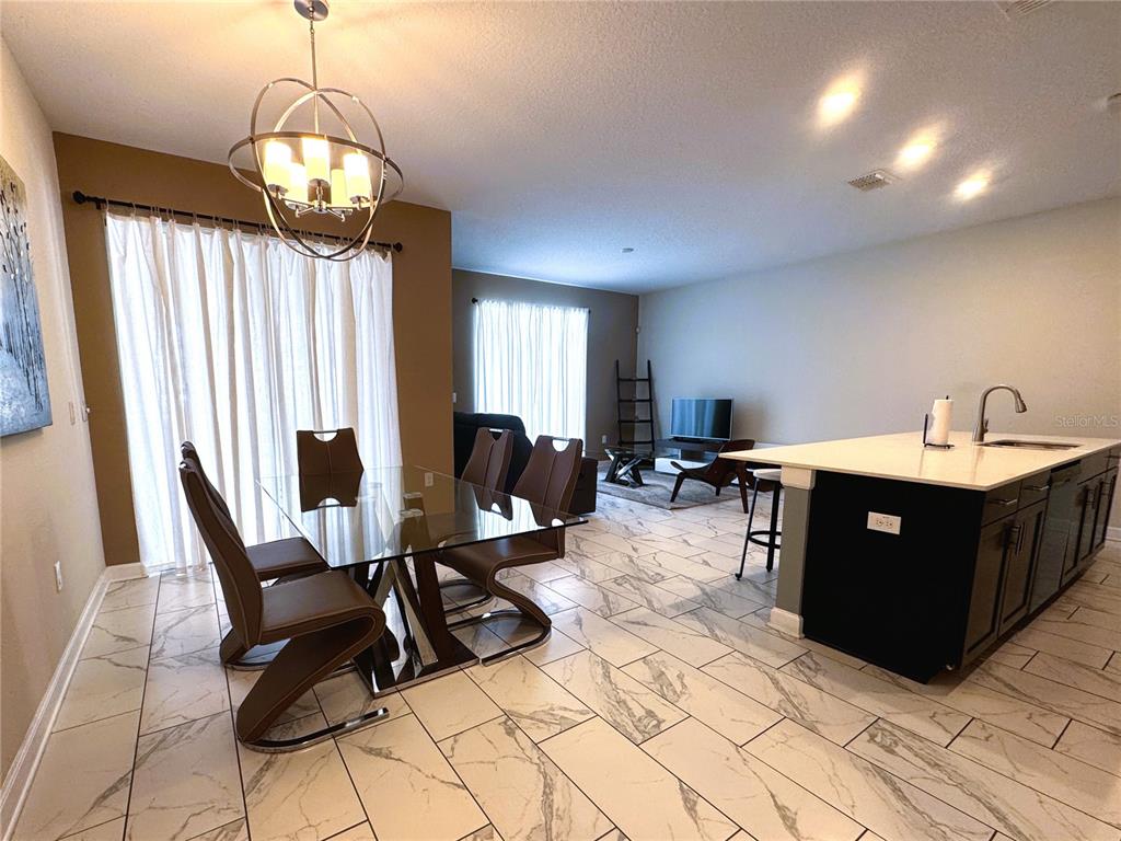 An open-concept kitchen and dining area features a glass table, marble-look tile, and pendant lighting — 1555 SANDBAGGER DRIVE, DAVENPORT, FL