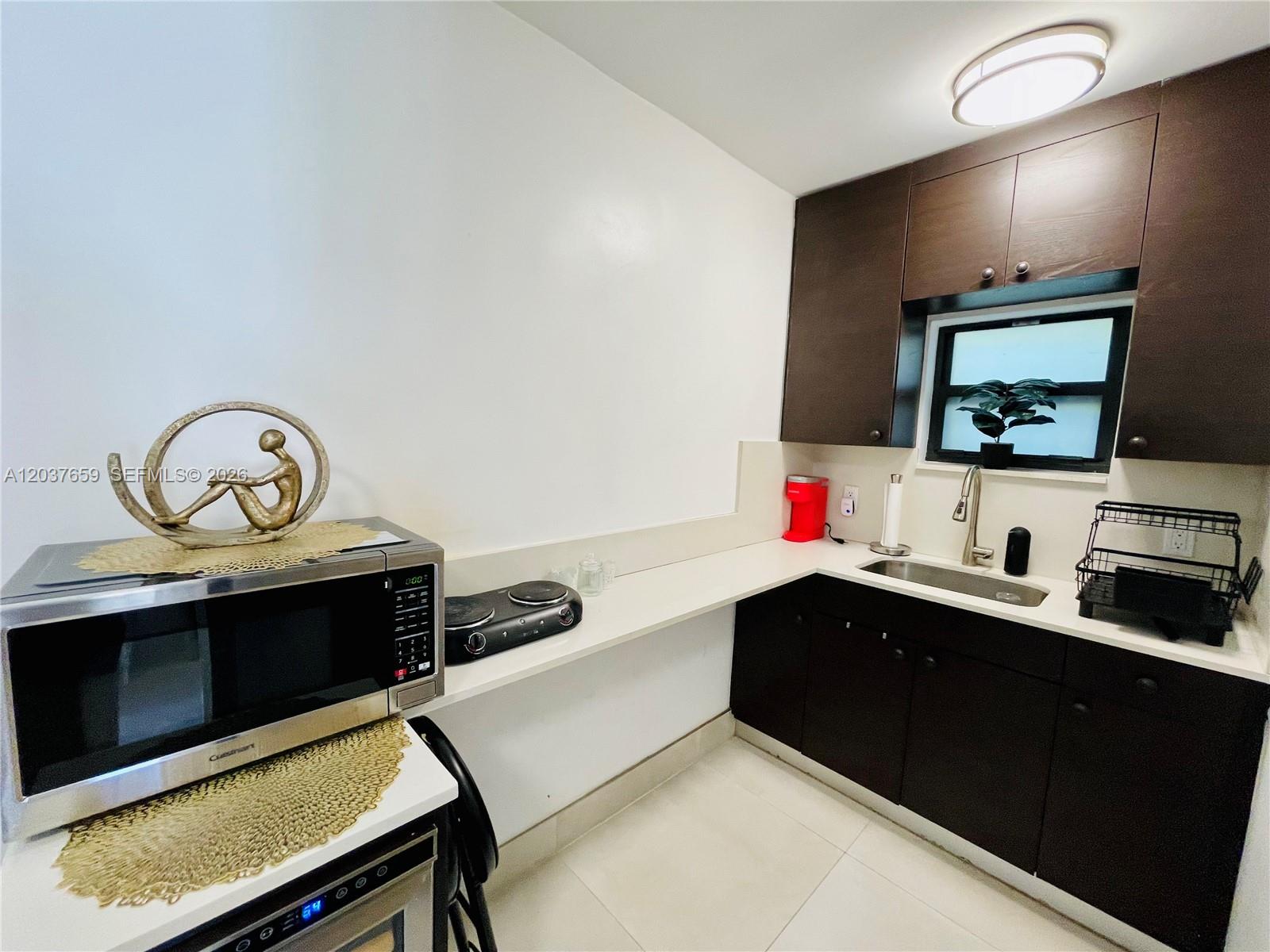 A small kitchen features dark wood cabinets, white countertops, a sink, and a microwave — 38 NW 52nd St # 1, Miami FL 33127, MIAMI, FL