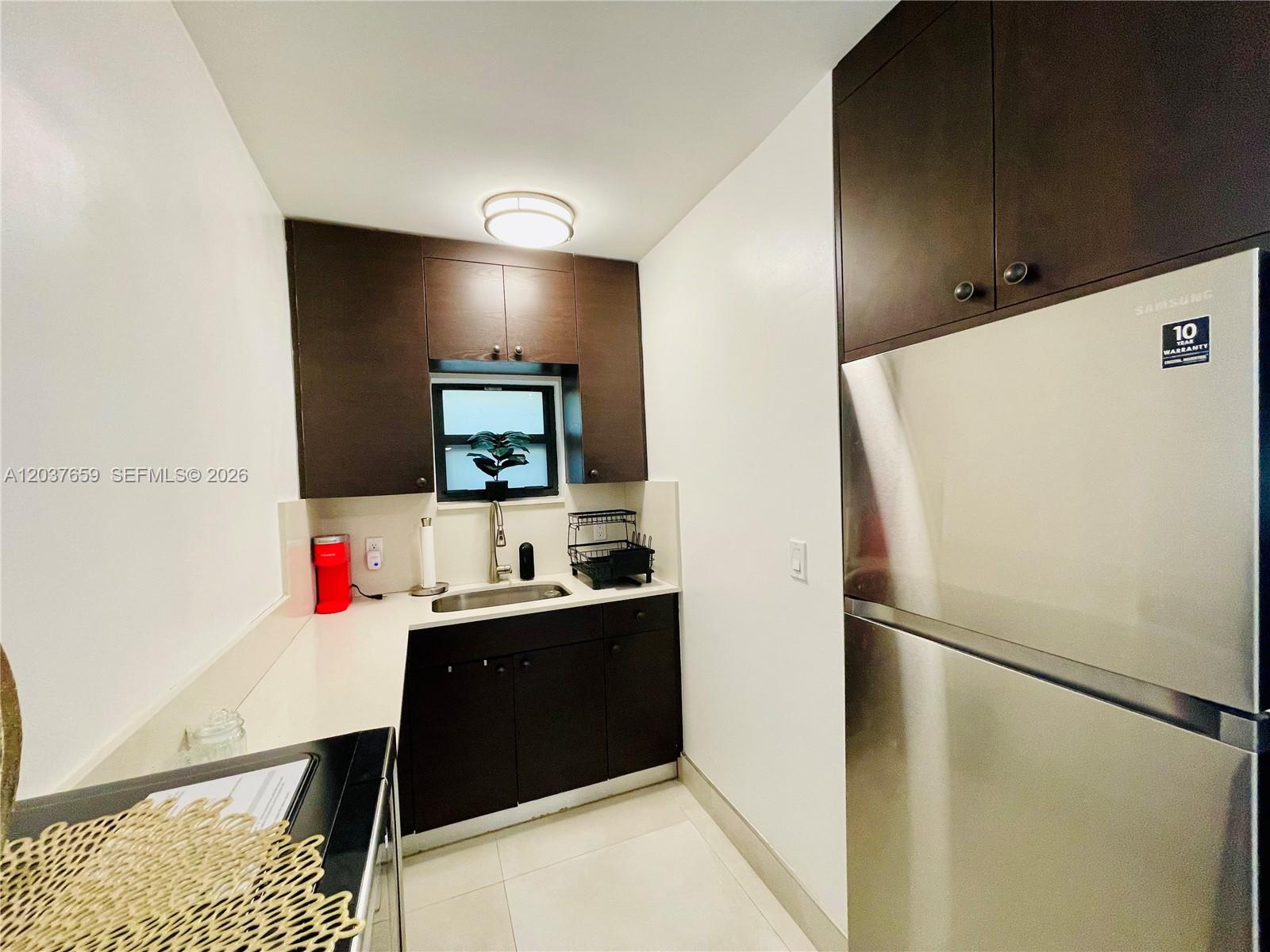 A small kitchen features dark wood cabinets, stainless steel appliances, and white countertops — 38 NW 52nd St # 1, Miami FL 33127, MIAMI, FL