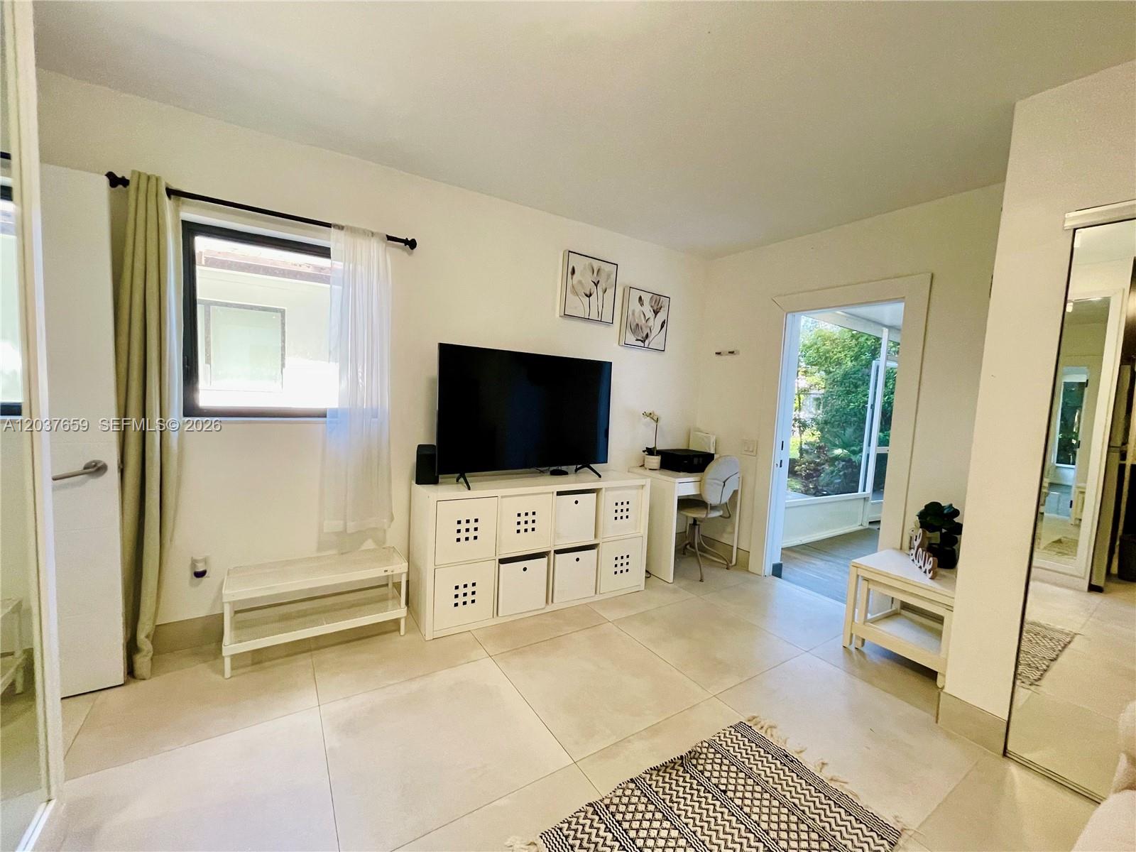 A bright room features a television on a storage unit, a desk, and tiled floors — 38 NW 52nd St # 1, Miami FL 33127, MIAMI, FL