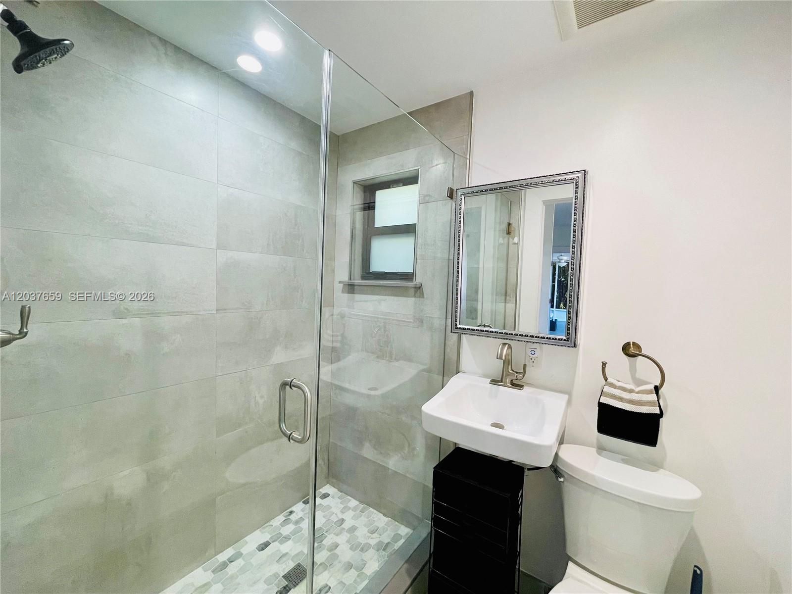 A modern bathroom features a glass-enclosed shower, a wall-mounted sink, and a toilet — 38 NW 52nd St # 1, Miami FL 33127, MIAMI, FL
