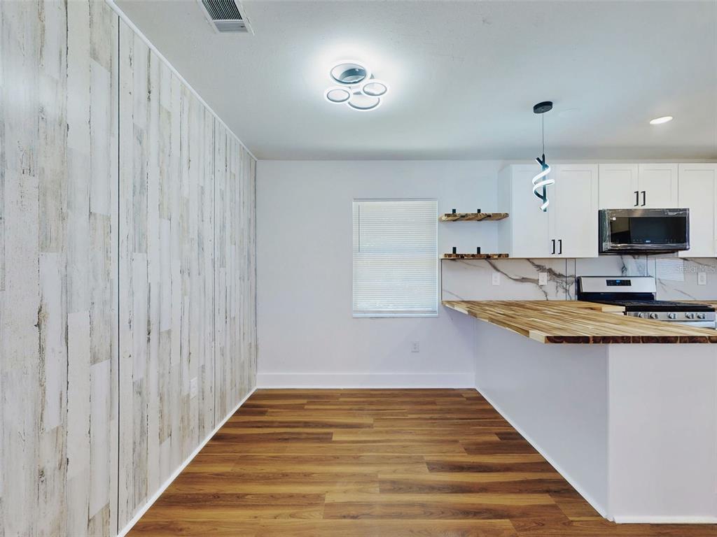 A kitchen and dining area with wood-look flooring, white cabinets, and a wood countertop island — 410 INWOOD AVENUE, NEW SMYRNA BEACH, FL