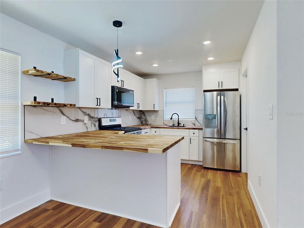 A kitchen features white cabinets, wood countertops, a marble backsplash, and stainless steel appliances — 410 INWOOD AVENUE, NEW SMYRNA BEACH, FL