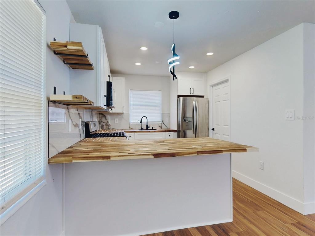 A kitchen features a wooden breakfast bar, open shelving, white cabinets, and stainless steel appliances — 410 INWOOD AVENUE, NEW SMYRNA BEACH, FL