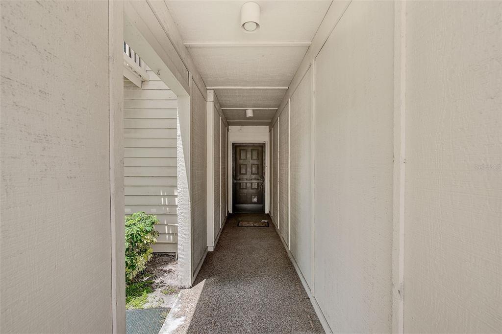 A covered outdoor walkway leads to a dark brown front door with a textured floor — 6435 92ND PLACE N UNIT 902, PINELLAS PARK, FL
