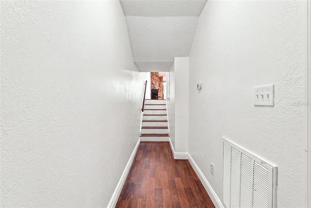 A hallway with wood-look flooring leads to a short staircase with a stone fireplace beyond — 6435 92ND PLACE N UNIT 902, PINELLAS PARK, FL
