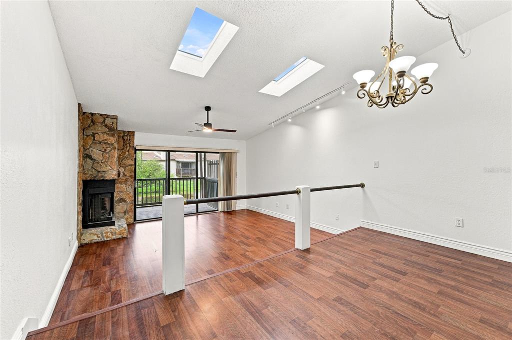 A living room with wood-look flooring, a stone fireplace, two skylights, and a chandelier — 6435 92ND PLACE N UNIT 902, PINELLAS PARK, FL