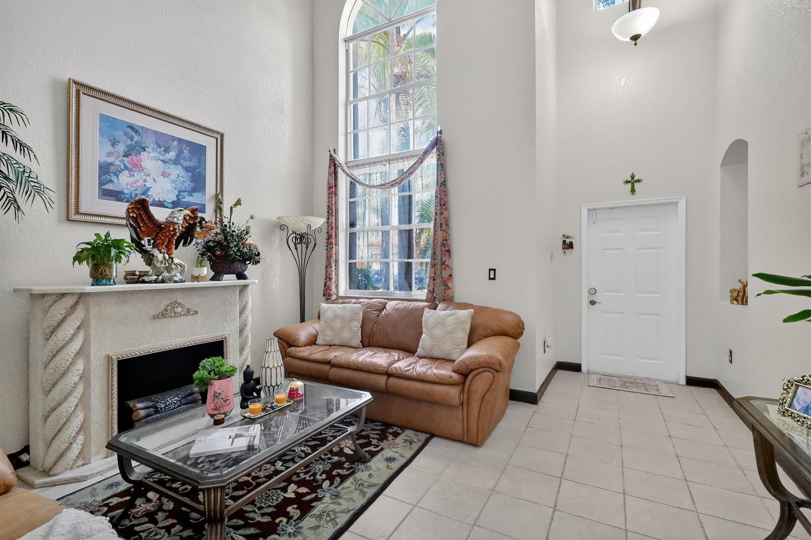 A living room features a fireplace, a leather sofa, a tall arched window, and tile flooring — 16266 SW 103rd Terrace, Miami FL 33196, MIAMI, FL