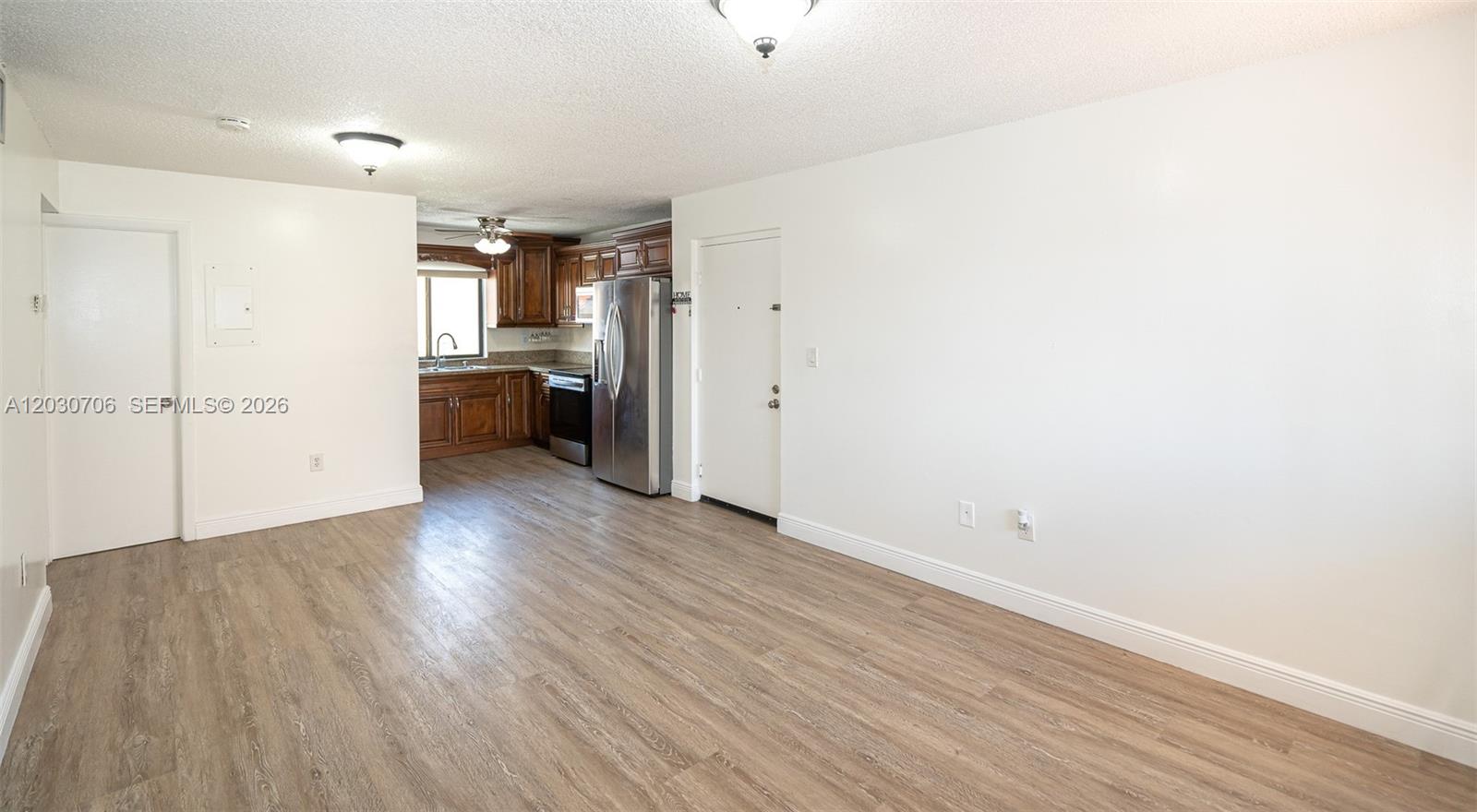 This open-concept living area features wood-look flooring, white walls, and an adjacent kitchen — 2740 W 62nd Pl # 201, Hialeah FL 33016, HIALEAH, FL