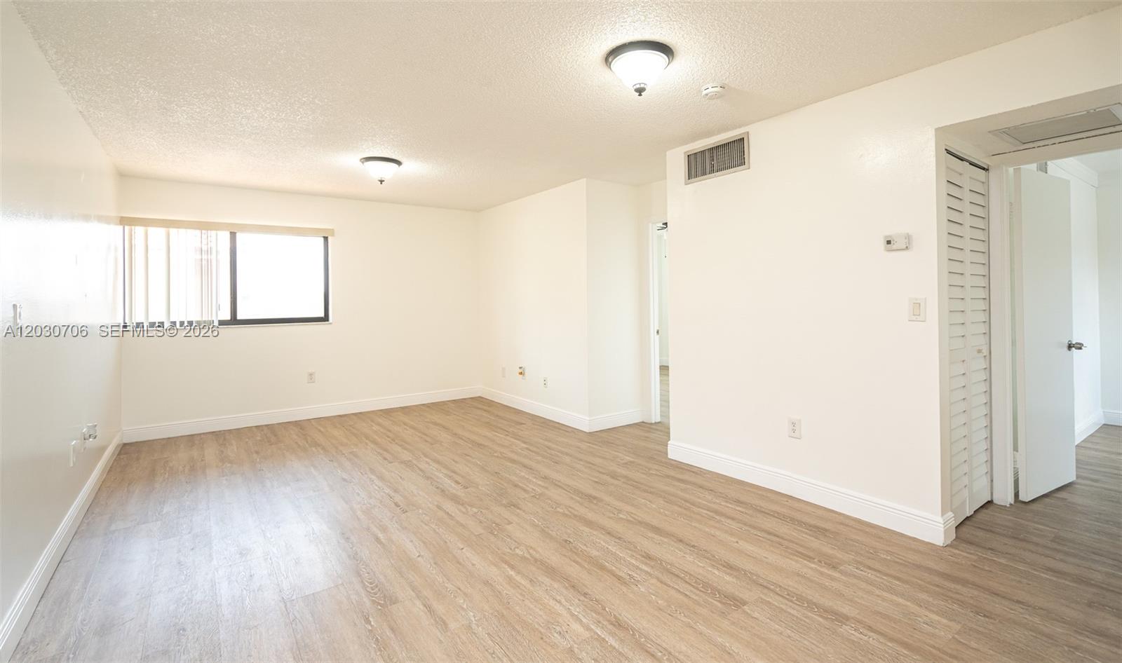 An empty room features light wood-look flooring, white walls, and two ceiling-mounted light fixtures — 2740 W 62nd Pl # 201, Hialeah FL 33016, HIALEAH, FL