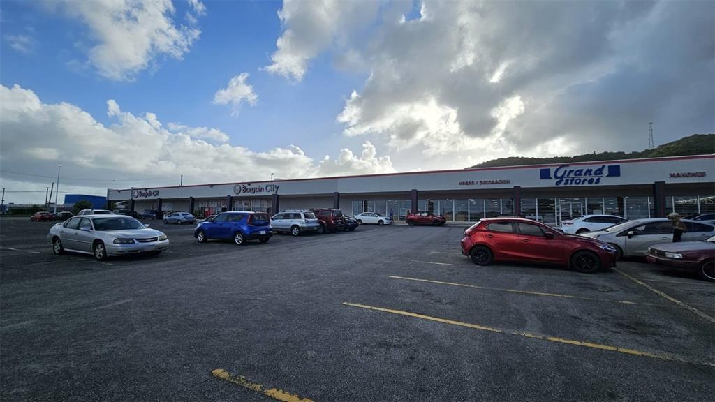 A parking lot sits in front of a strip mall with several retail store signs — Km 40.5 PR 3, FAJARDO, PR