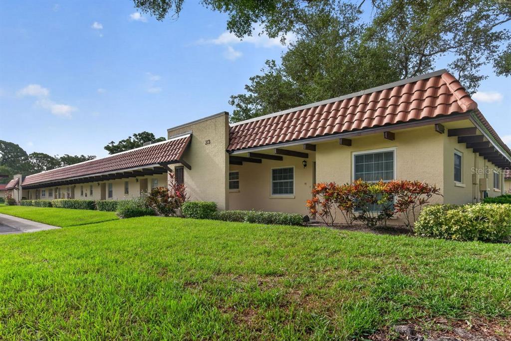 A long, single-story apartment building features a red tile roof and a grassy front lawn — 1701 PINEHURST ROAD UNIT 23G, DUNEDIN, FL
