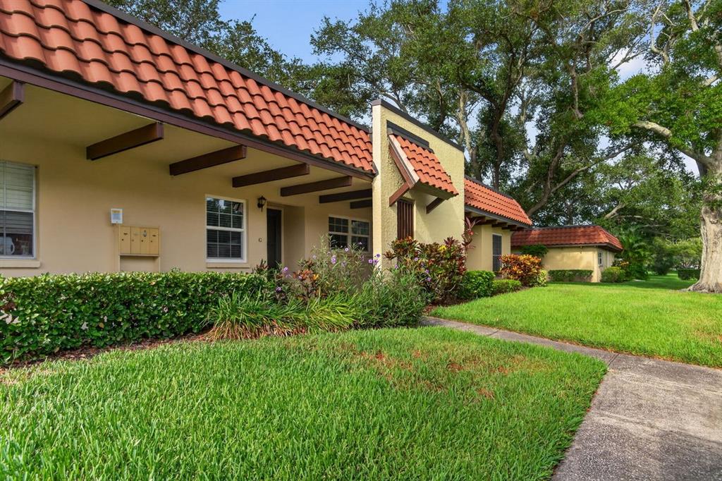 A single-story building with a terracotta tile roof, stucco walls, and a landscaped front yard — 1701 PINEHURST ROAD UNIT 23G, DUNEDIN, FL
