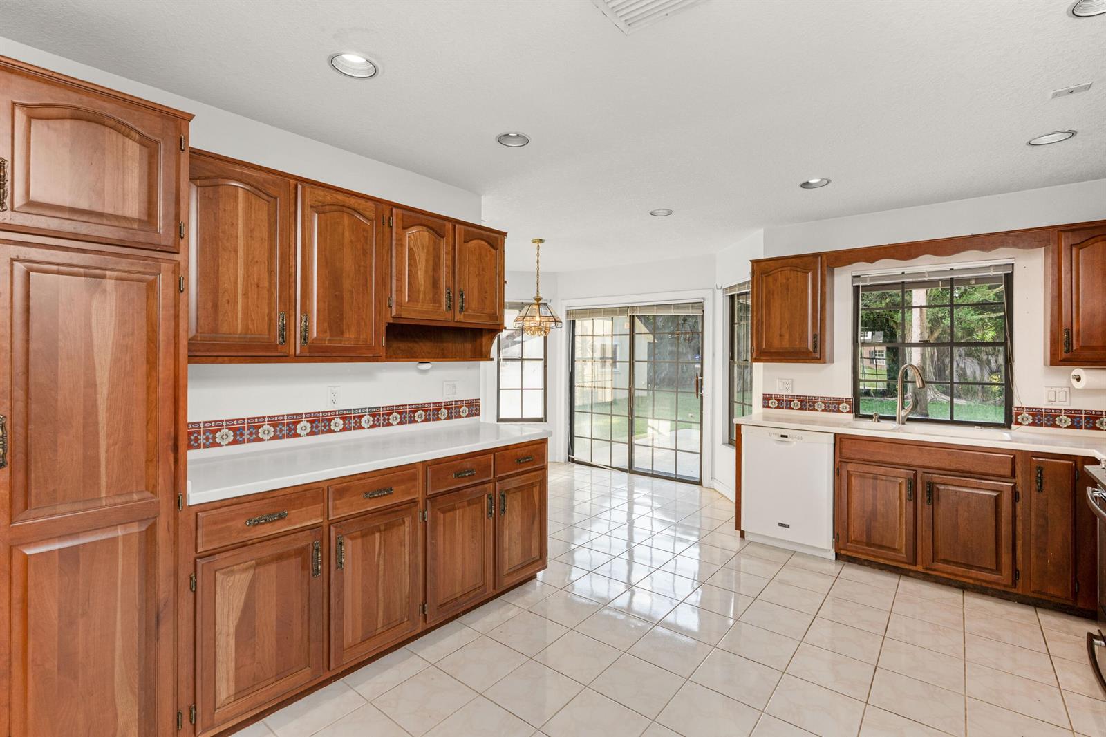 A kitchen features wood cabinets, white countertops, a tiled backsplash, and light-colored floor tiles — 3693 Valley Park Way, Lake Worth FL 33467, LAKE WORTH, FL