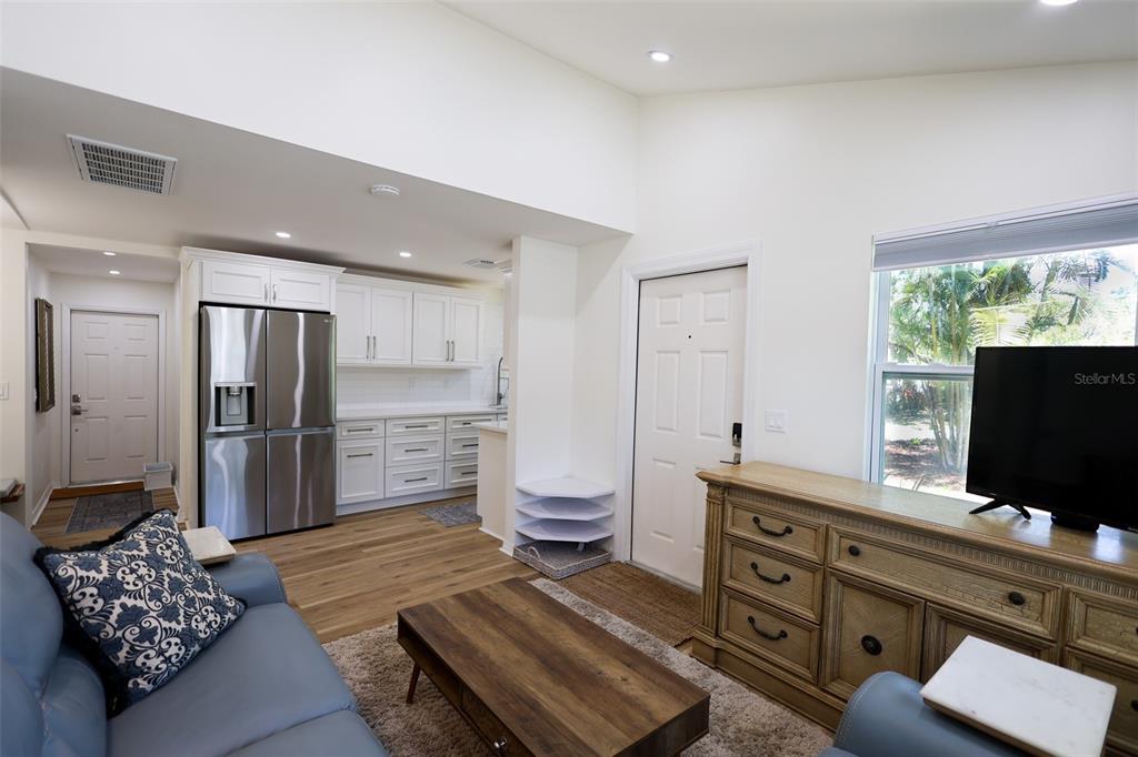 A living room with a television, wooden dresser, and an adjacent kitchen with white cabinets — 4501 70TH STREET N, ST PETERSBURG, FL