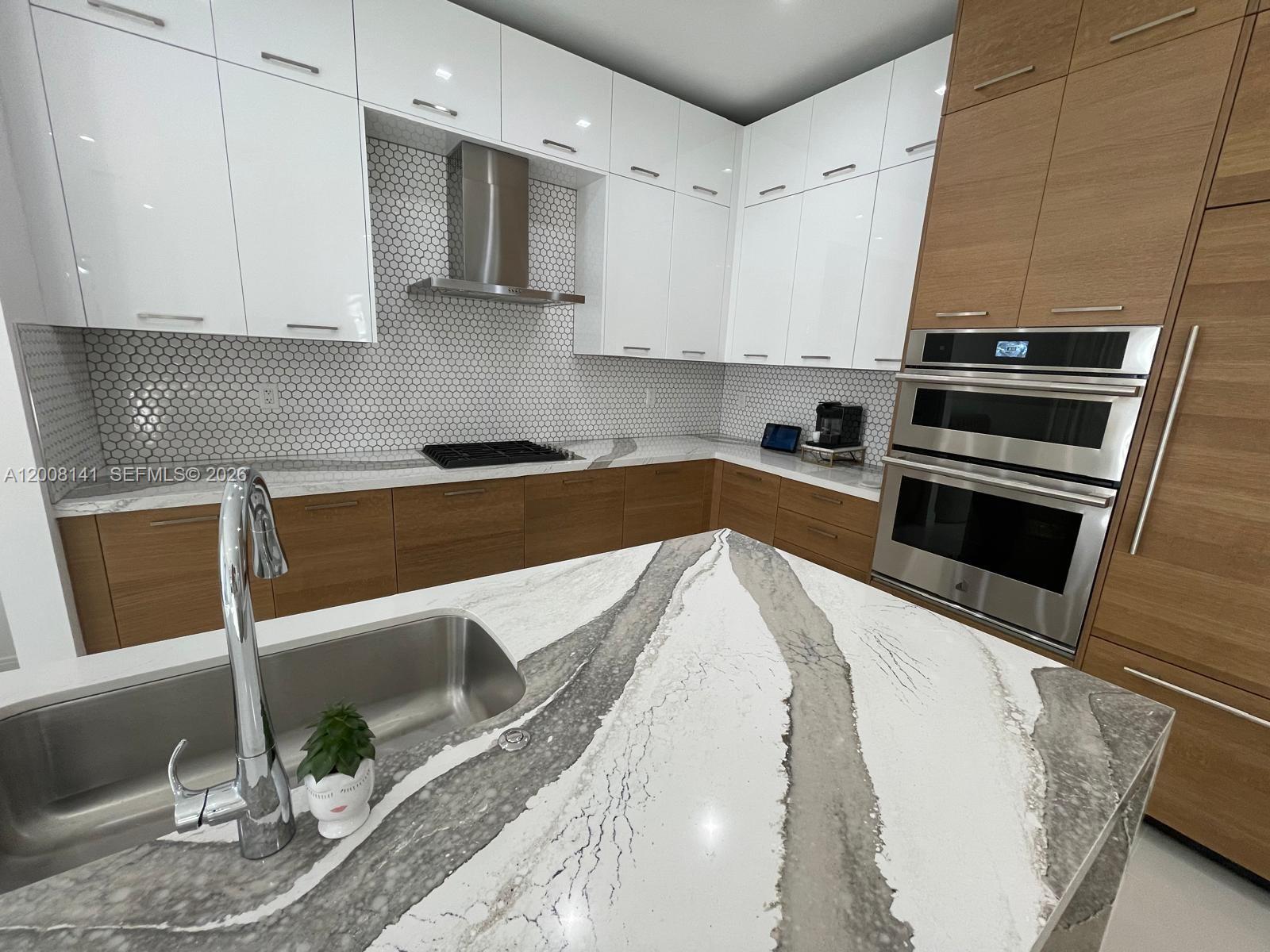 A modern kitchen features white upper cabinets, wood lower cabinets, and a marble-topped island — 8283 NW 44th St, Doral FL 33166, DORAL, FL