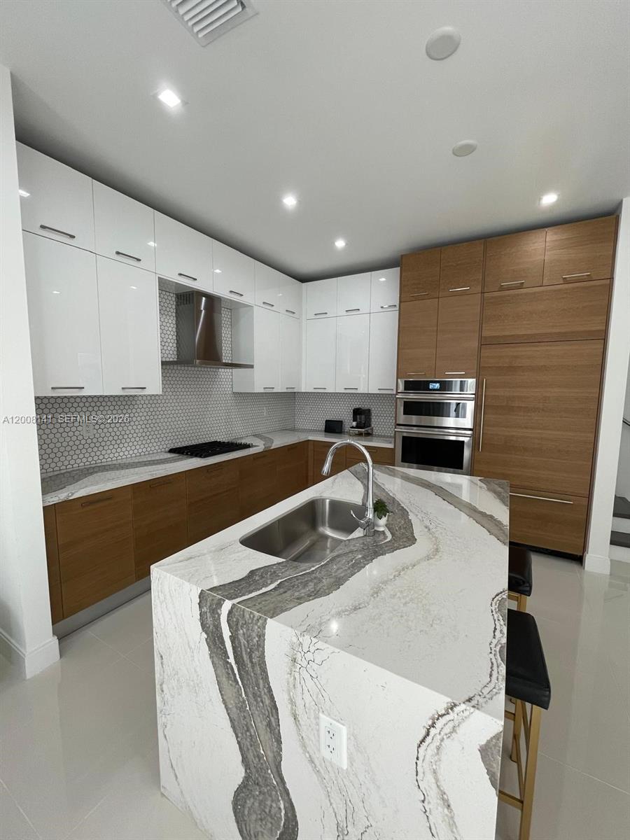A modern kitchen features white upper cabinets, wood lower cabinets, and a marble-topped island — 8283 NW 44th St, Doral FL 33166, DORAL, FL