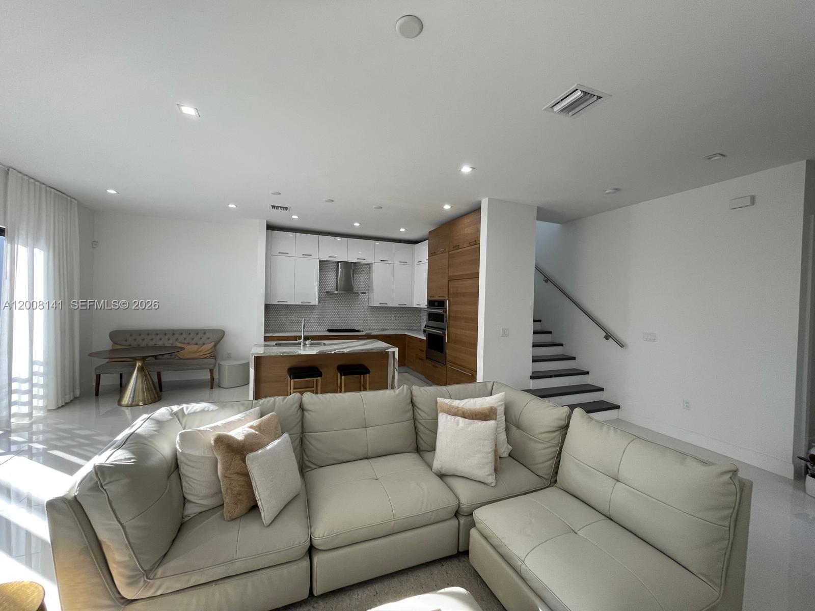 A modern open-concept living room features a kitchen with white and wood cabinetry — 8283 NW 44th St, Doral FL 33166, DORAL, FL
