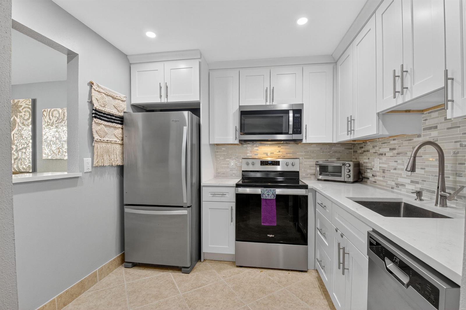 A kitchen features white cabinets, stainless steel appliances, a tiled backsplash, and light-colored countertops — 499 Monaco K # K, Delray Beach FL 33446, DELRAY BEACH, FL