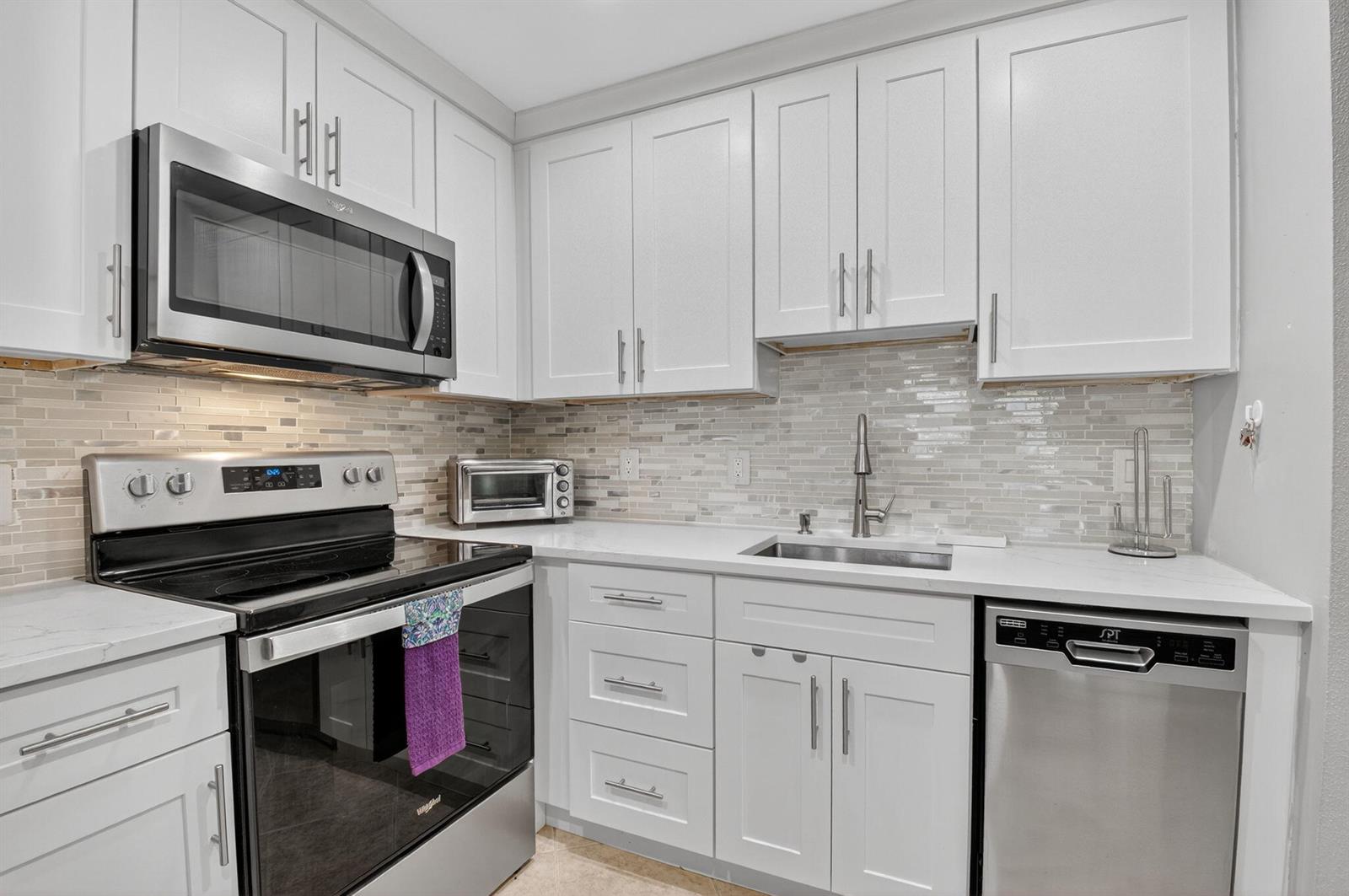 A kitchen with white cabinets, stainless steel appliances, and a light-colored tile backsplash — 499 Monaco K # K, Delray Beach FL 33446, DELRAY BEACH, FL