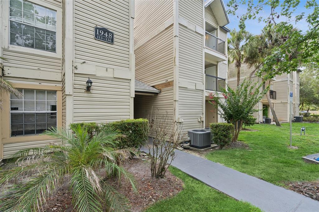Exterior view of a multi-story apartment building with beige siding and a concrete walkway — 1948 LAKE ATRIUMS CIRCLE UNIT 124, ORLANDO, FL