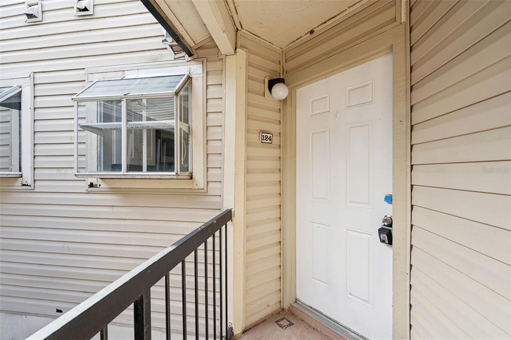 An exterior view of a residential unit entrance with beige siding and a white door — 1948 LAKE ATRIUMS CIRCLE UNIT 124, ORLANDO, FL