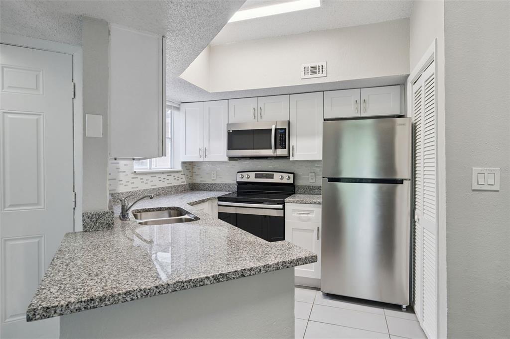 A kitchen features white cabinets, granite countertops, stainless steel appliances, and a tiled floor — 1948 LAKE ATRIUMS CIRCLE UNIT 124, ORLANDO, FL