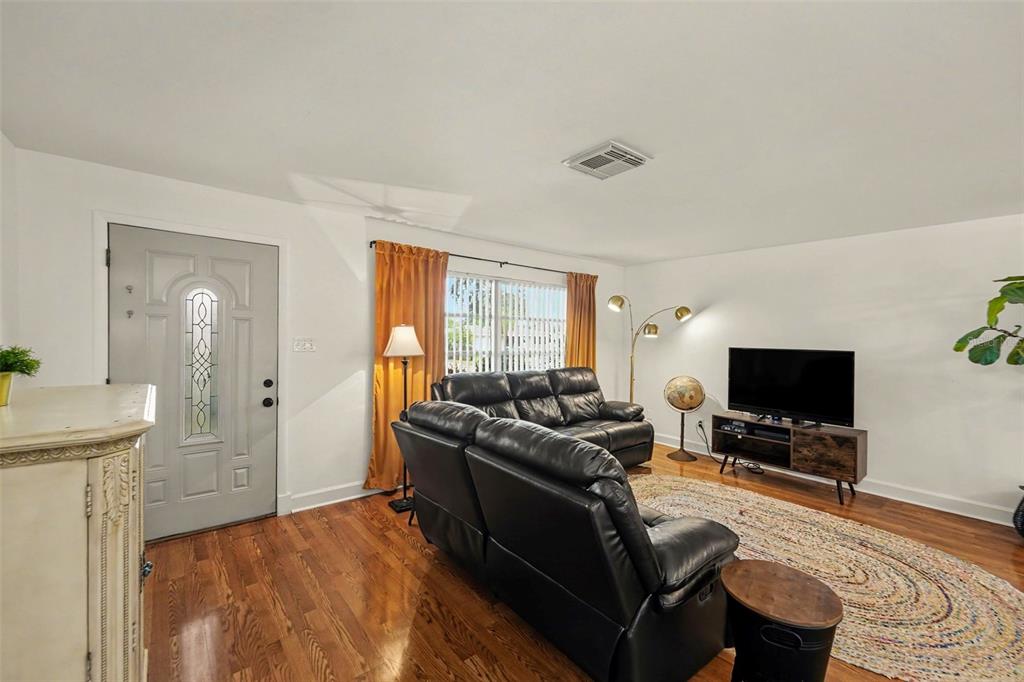 A living room features hardwood floors, a black leather sofa, a television, and a front door — 1251 OAKVIEW AVENUE, CLEARWATER, FL