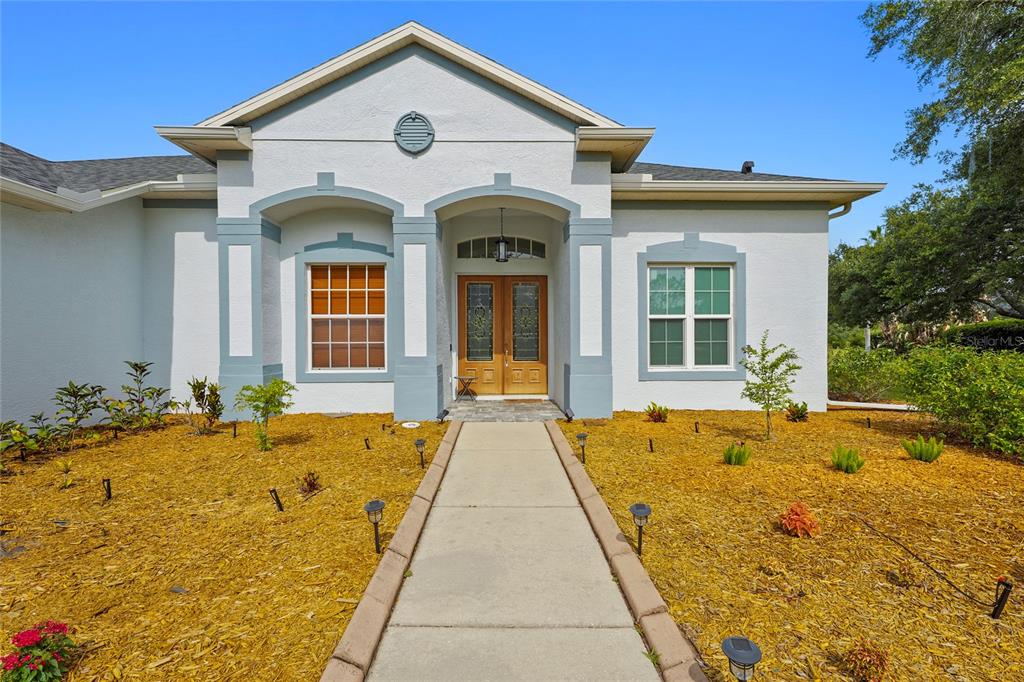 A single-story house with a light-colored stucco exterior, double front doors, and a concrete walkway — 8018 SNOWY EGRET PLACE, BRADENTON, FL