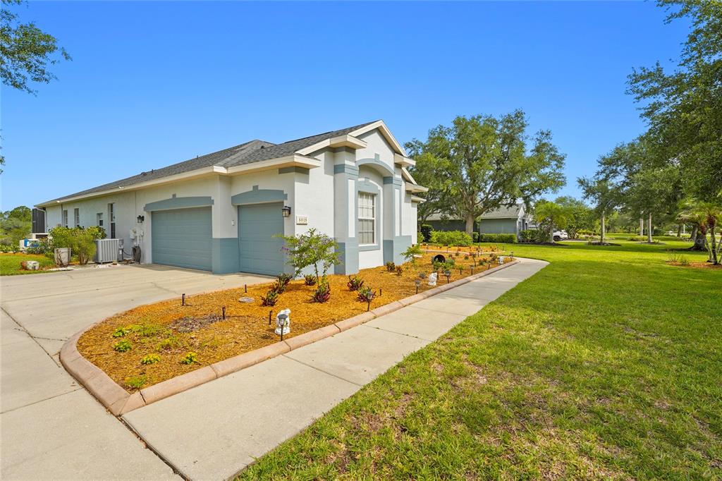 A single-story house with a two-car garage, light-colored stucco walls, and a landscaped front yard — 8018 SNOWY EGRET PLACE, BRADENTON, FL