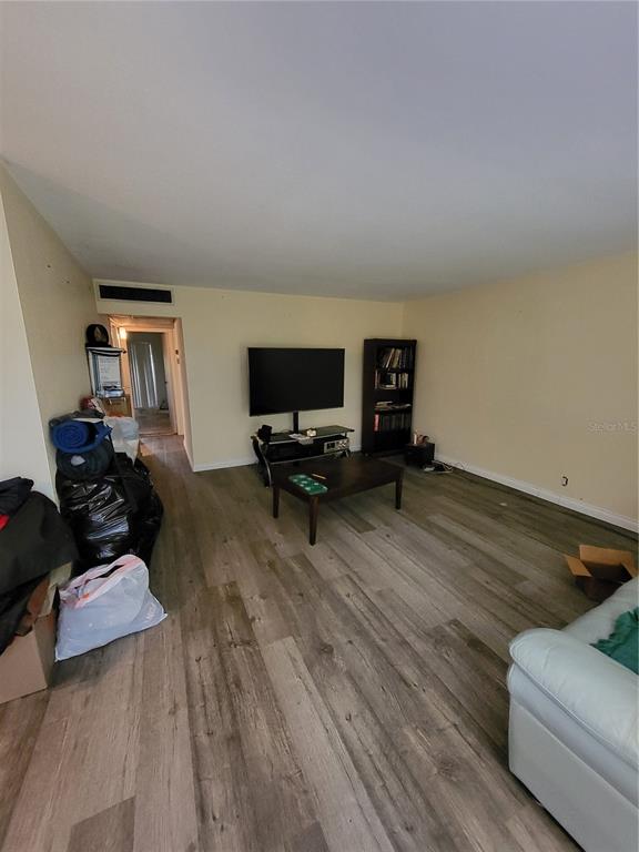 A living room features light-colored walls, wood-look flooring, a television on a stand, and shelving — 202 BEDFORD TRAIL UNIT 97, SUN CITY CENTER, FL