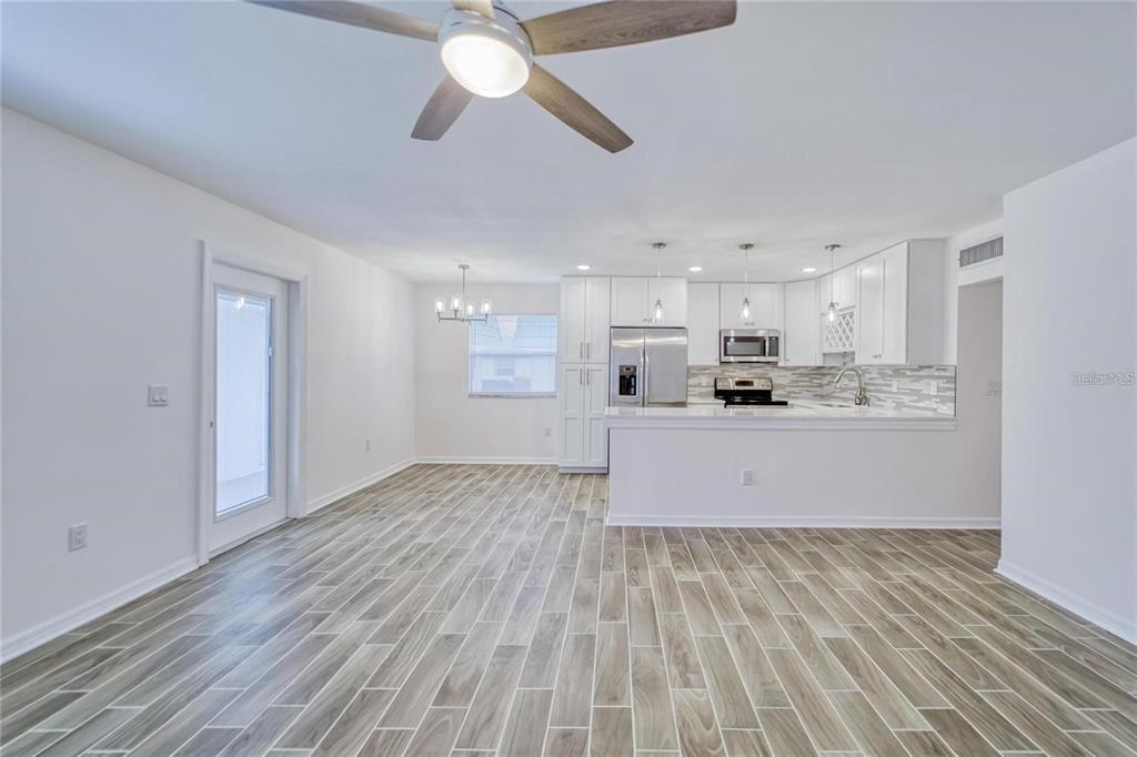 An open-concept kitchen and dining area features white cabinets, stainless steel appliances, and wood-look flooring — 202 BEDFORD TRAIL UNIT 97, SUN CITY CENTER, FL