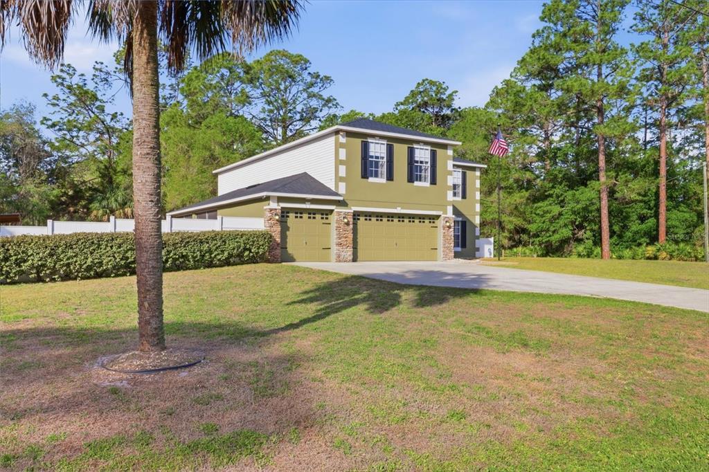A two-story house with olive green siding, stone accents, and a three-car garage — 9508 N DAWNFLOWER AVENUE, CRYSTAL RIVER, FL