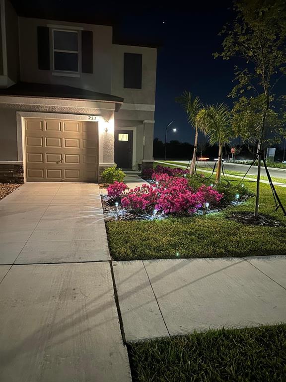 A two-story house exterior at night features a garage, a sidewalk, and illuminated pink bushes — 253 TULIP BANDED WAY, RUSKIN, FL