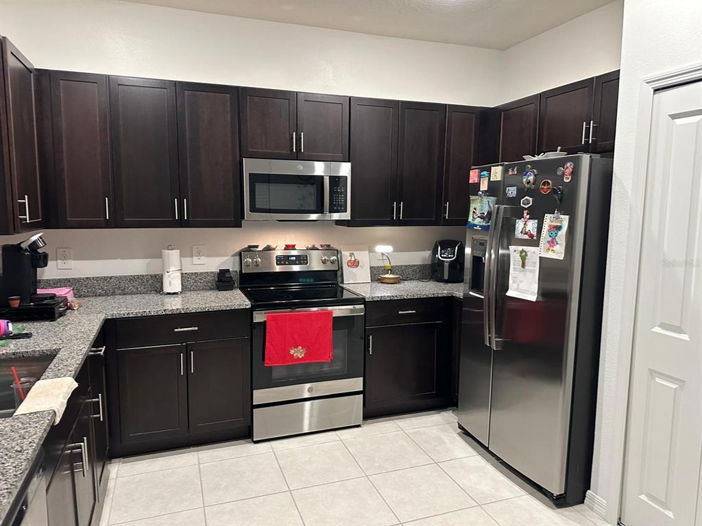 A kitchen features dark wood cabinets, granite countertops, and stainless steel appliances — 253 TULIP BANDED WAY, RUSKIN, FL