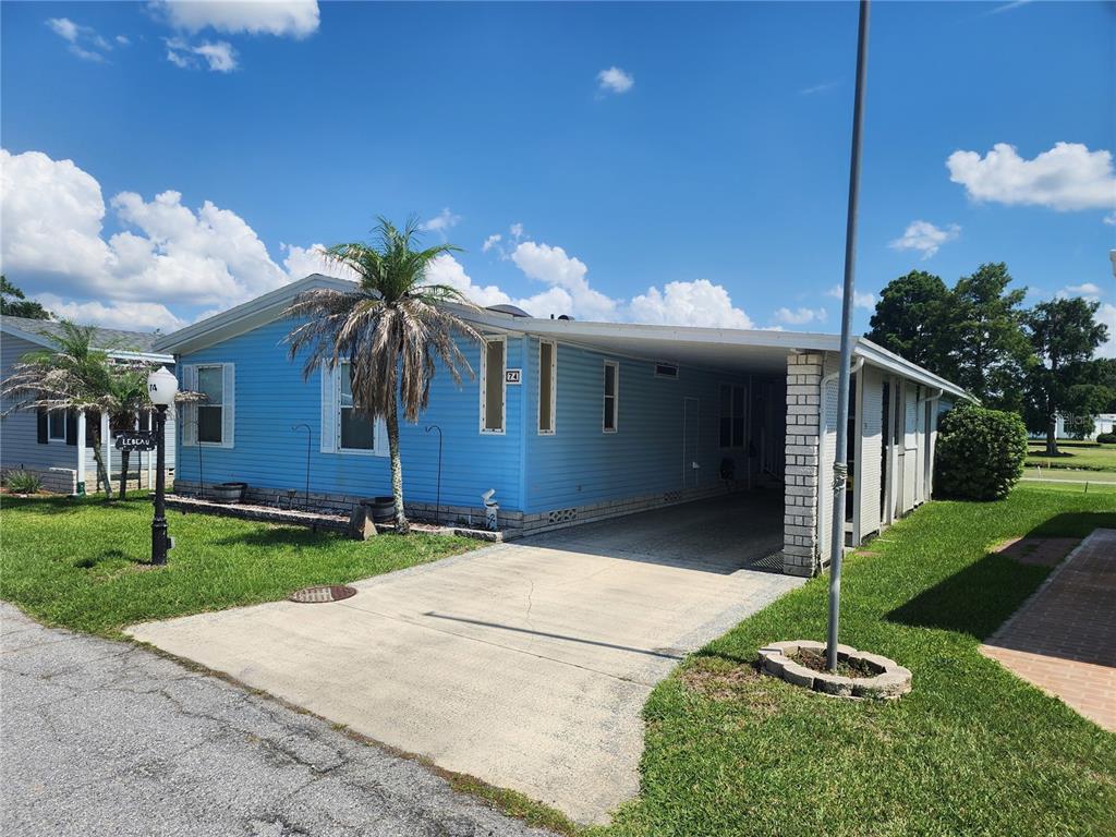 A light blue manufactured home features a concrete driveway, a carport, and a palm tree — 74 STRAPHMORE DRIVE, HAINES CITY, FL