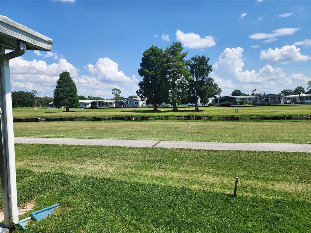 A view of a grassy lawn, a paved path, and distant houses under a blue sky — 74 STRAPHMORE DRIVE, HAINES CITY, FL