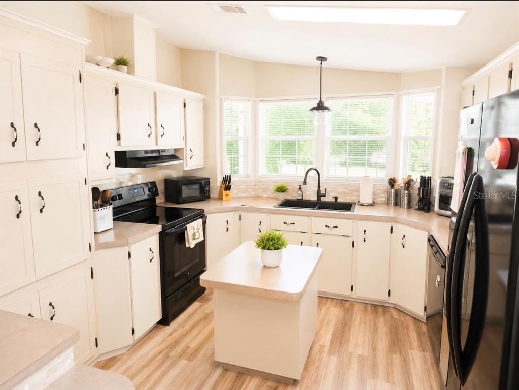 A kitchen with white cabinets, black appliances, a central island, and light wood-look flooring — 74 STRAPHMORE DRIVE, HAINES CITY, FL