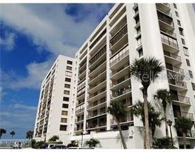 A low-angle exterior view of a tall, white multi-story residential building with balconies and palm trees — 1460 GULF BOULEVARD UNIT 411, CLEARWATER BEACH, FL