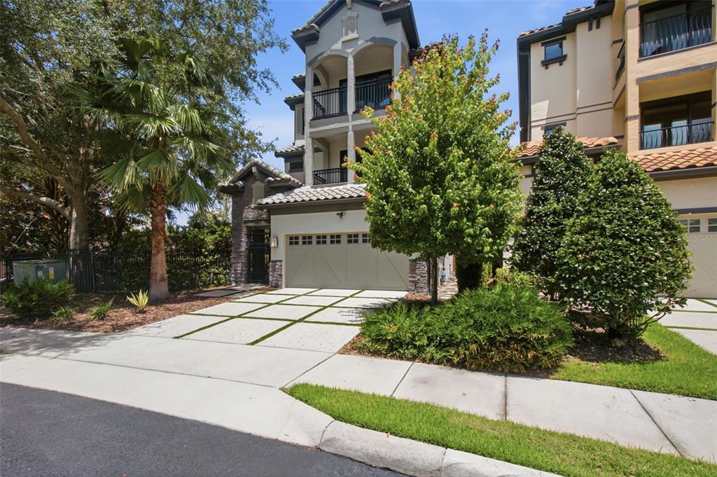 A multi-story house with a beige garage, a paved driveway, and surrounding trees and landscaping — 7689 TOSCANA BOULEVARD, ORLANDO, FL