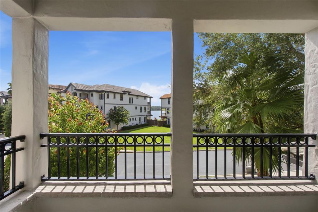 A balcony with black metal railings overlooks a grassy courtyard, apartment buildings, and a lake — 7689 TOSCANA BOULEVARD, ORLANDO, FL