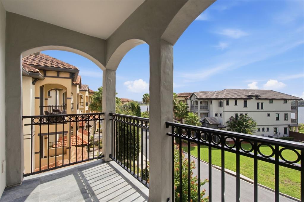 A covered balcony with black metal railings overlooks a residential street and nearby apartment buildings — 7689 TOSCANA BOULEVARD, ORLANDO, FL