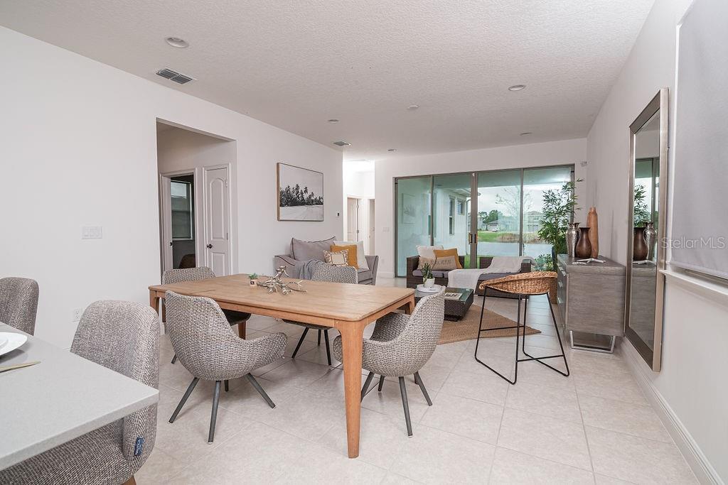An open-concept dining and living area features tile flooring, a wooden table, and sliding doors — 7508 WING SPAN WAY, ST CLOUD, FL