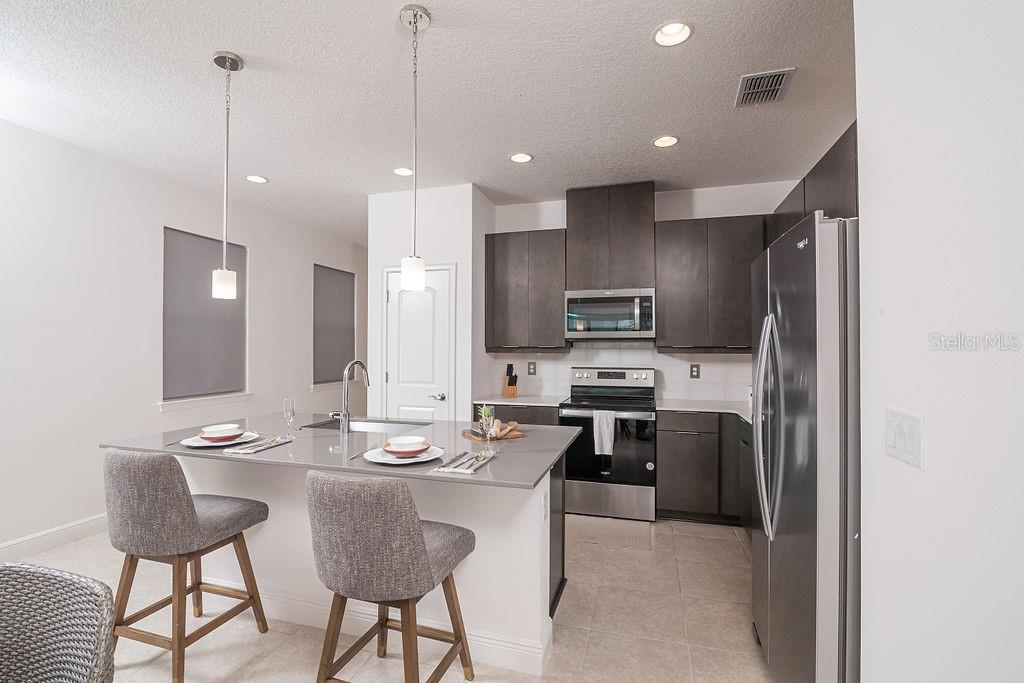 A modern kitchen features dark cabinetry, stainless steel appliances, and a gray-topped island with seating — 7508 WING SPAN WAY, ST CLOUD, FL