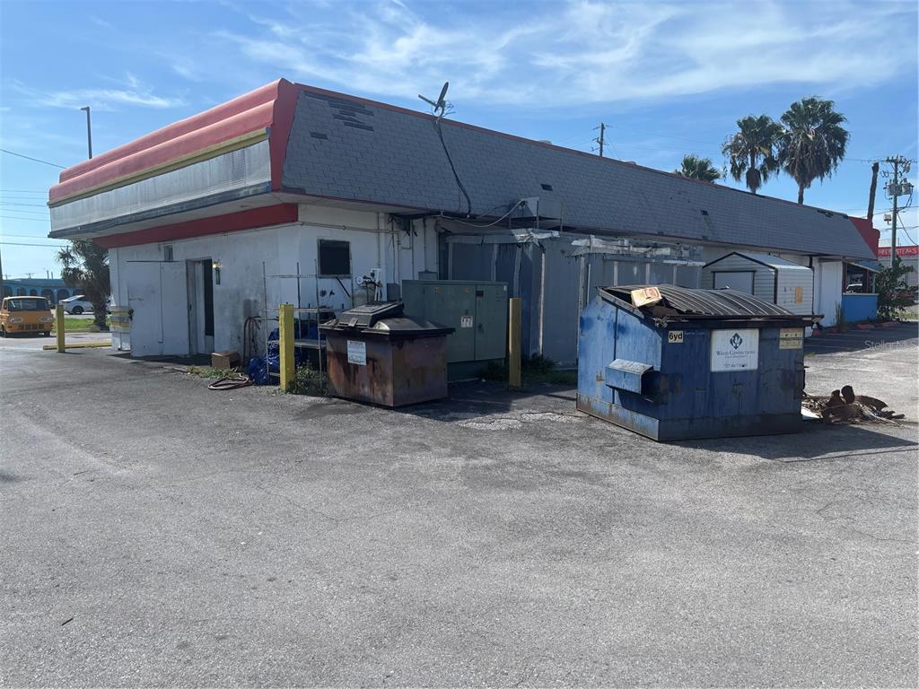 The exterior of a commercial building features a red-trimmed roof, dumpsters, and a paved lot — 1730 US HIGHWAY 19, HOLIDAY, FL