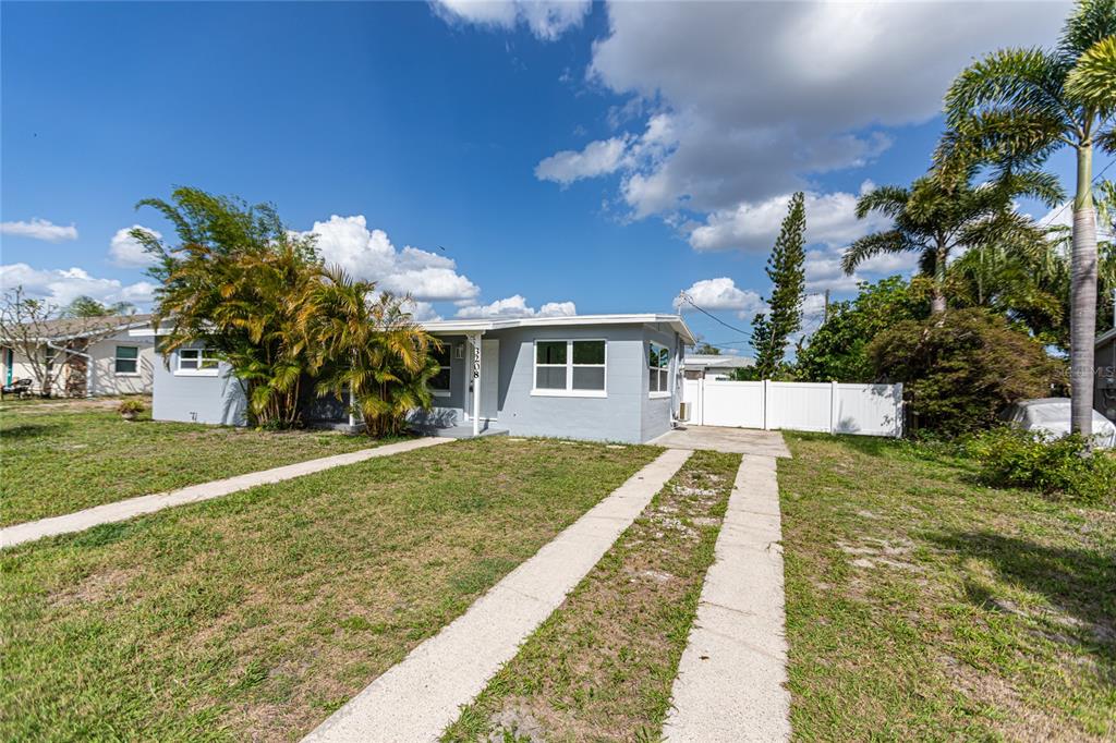 A single-story gray house with a concrete driveway and palm trees under a blue sky — 3208 PINETREE STREET, PORT CHARLOTTE, FL